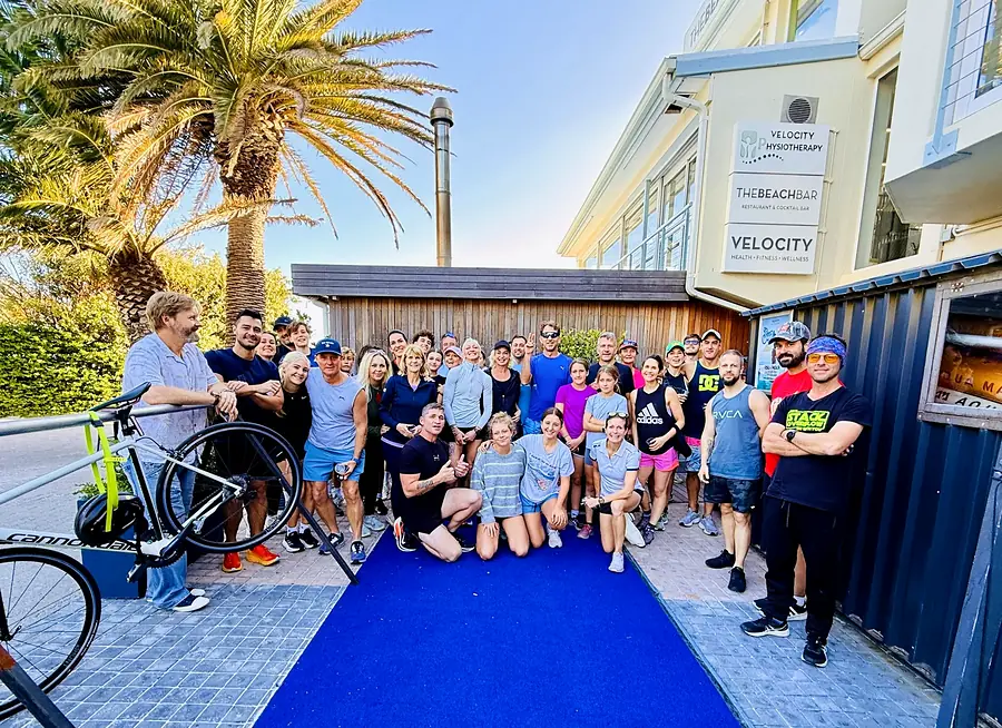 A big group of Velocity members outside the white clapboard gym building on a sunny morning