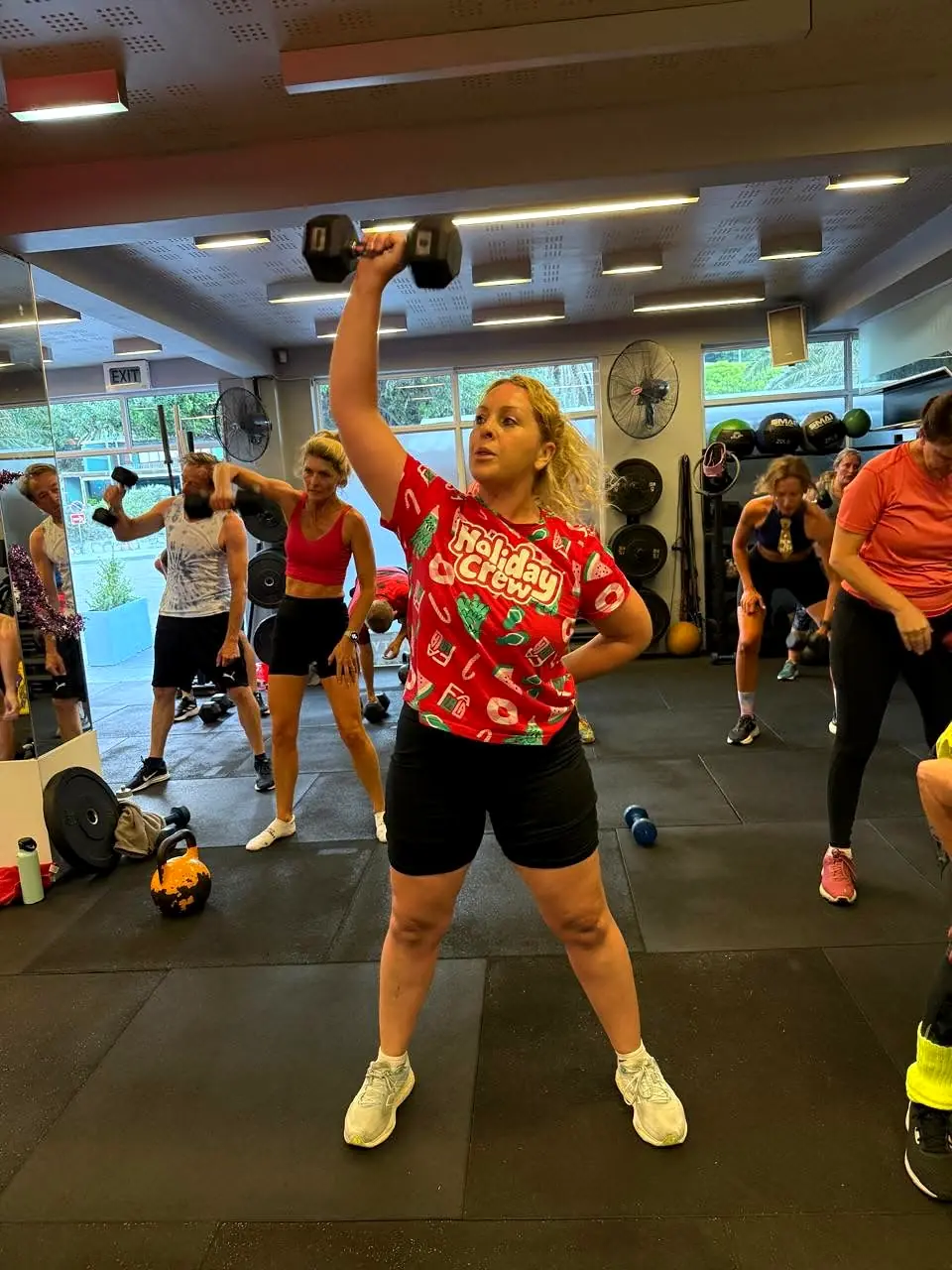 A member pressing a dumbbell overhead in a festive class